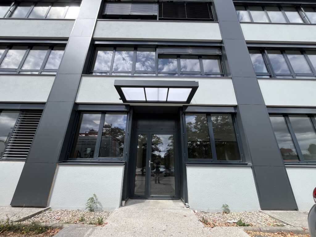 Marquise aluminium sur mesure sans poteaux avec tirants inox au-dessus d’une entrée secondaire professionnelle à Besançon.