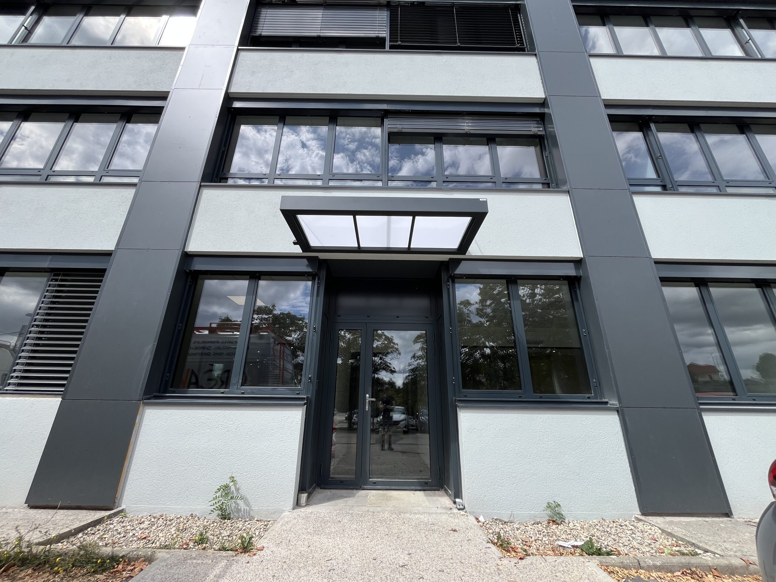 Marquise aluminium sur mesure sans poteaux avec tirants inox au-dessus d’une entrée secondaire professionnelle à Besançon.
