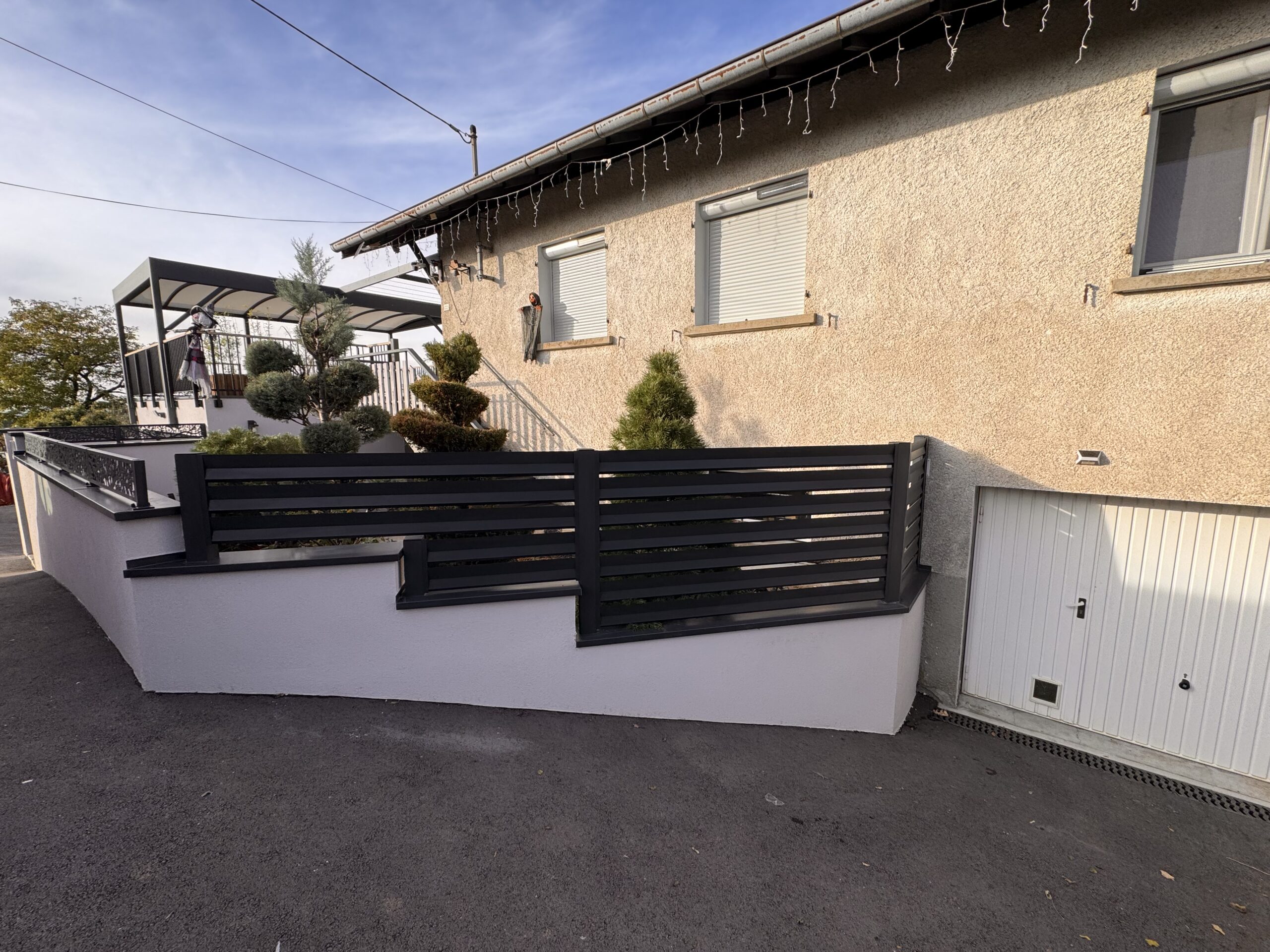Clôture aluminium gris anthracite à lames horizontales posée sur les murets extérieurs d'une maison.